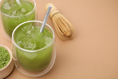 Photo of Delicious iced green matcha tea, powder and bamboo whisk on pale brown background, closeup. Space for text