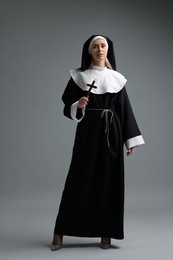Woman in nun habit holding wooden cross on grey background