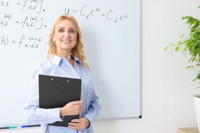 Happy professor with clipboard near whiteboard in classroom