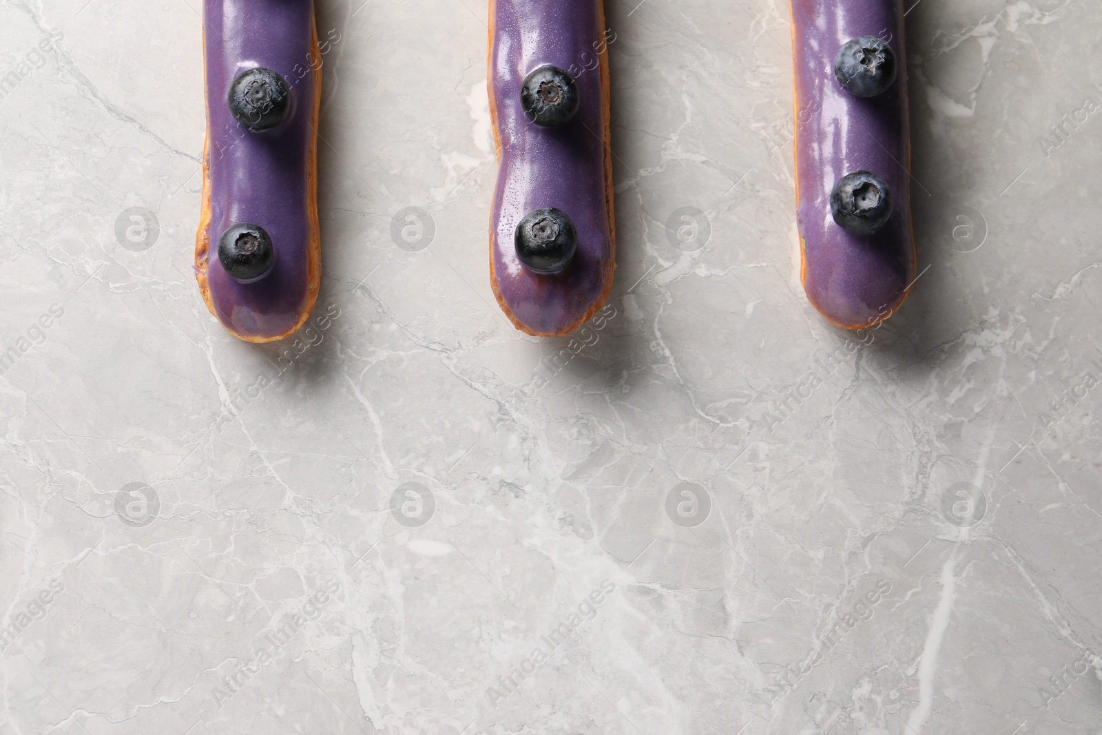 Photo of Tasty glazed eclairs with blueberries on grey marble table, flat lay. Space for text