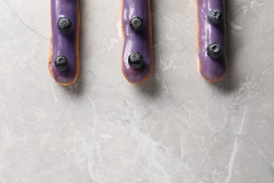 Tasty glazed eclairs with blueberries on grey marble table, flat lay. Space for text