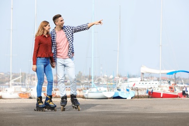 Happy lovely couple roller skating on embankment. Space for text