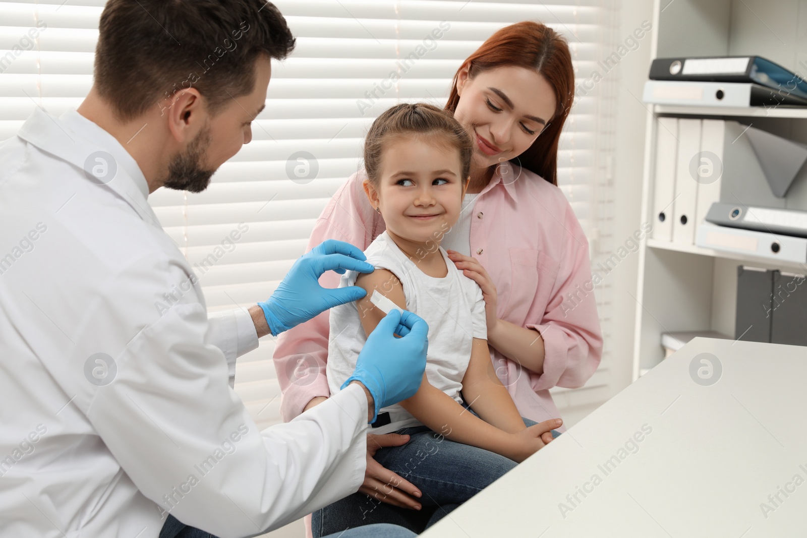 Photo of Children's hepatitis vaccination. Mother with her daughter in clinic. Doctor sticking medical plaster on little girl's arm