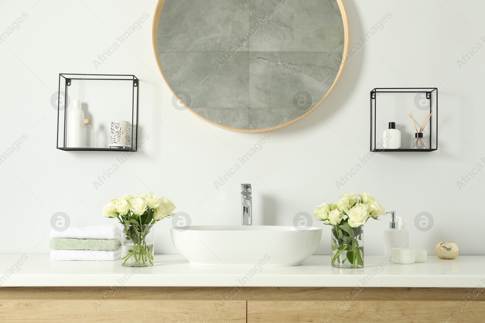 Photo of White sink between beautiful roses and toiletries in bathroom