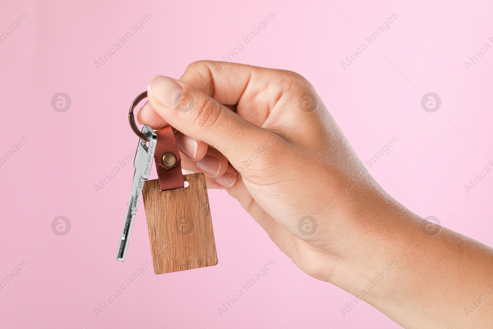 Photo of Woman holding key with wooden keychain on pink background, closeup