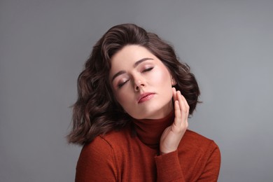 Portrait of beautiful young woman with wavy hairstyle on grey background