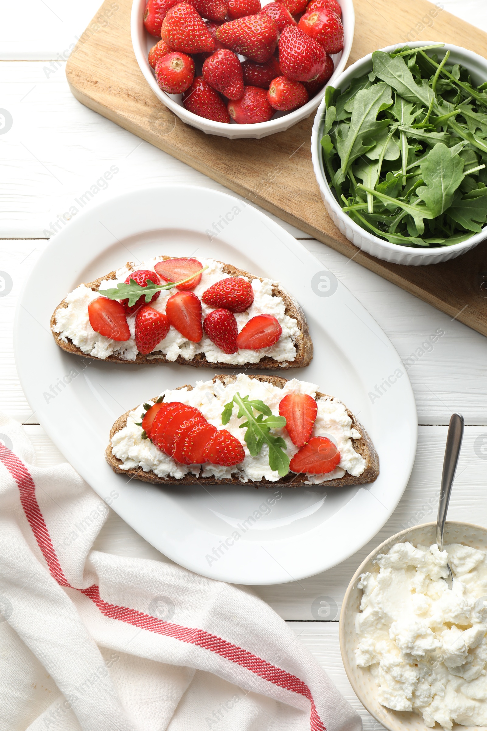 Photo of Delicious ricotta bruschettas with strawberry and arugula on white wooden table, flat lay