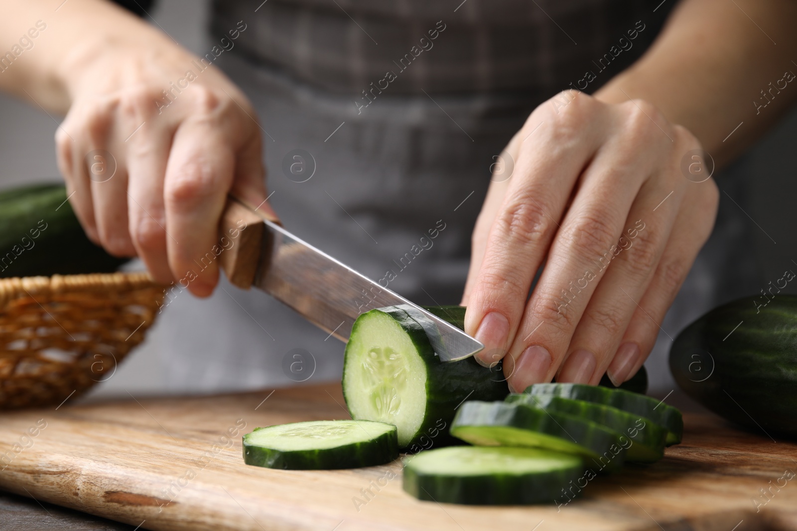 Photo of Woman cutting fresh cucumber at table, closeup