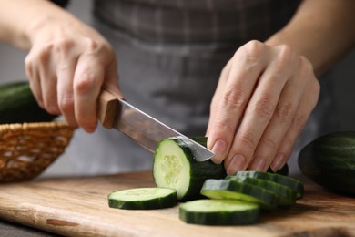 Woman cutting fresh cucumber at table, closeup