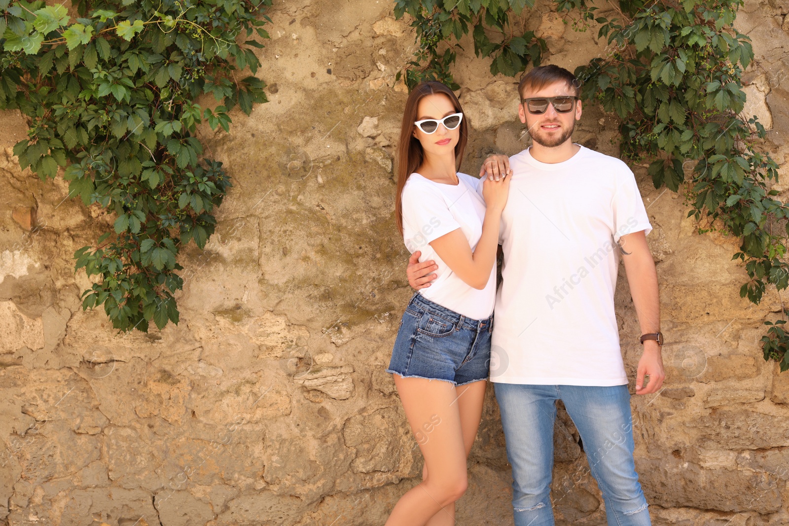 Photo of Young couple wearing white t-shirts near stone wall on street