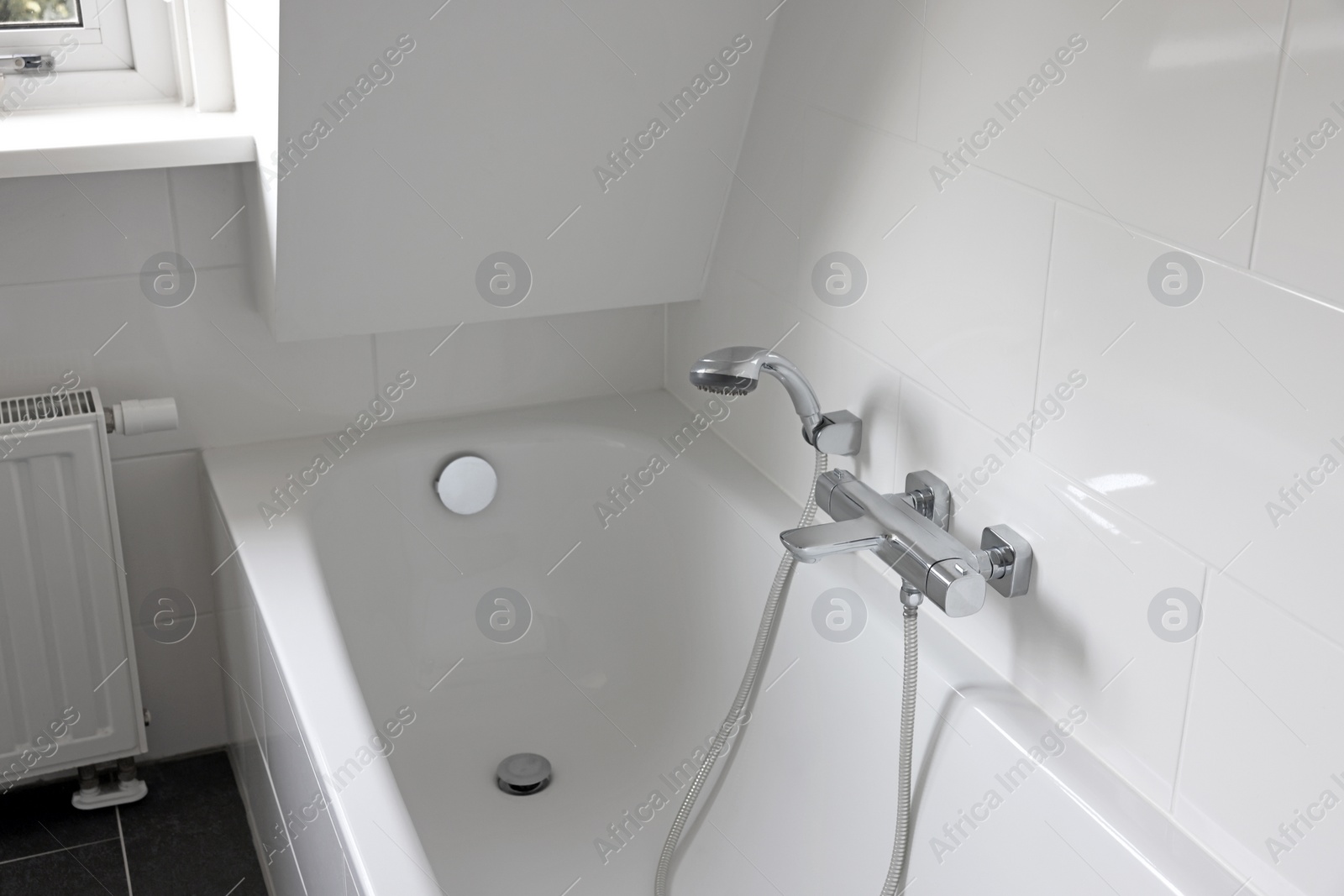 Photo of Clean tub with showerhead and tap in white bathroom. Interior design