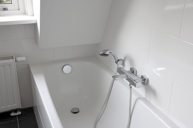 Clean tub with showerhead and tap in white bathroom. Interior design