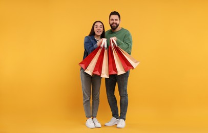 Photo of Happy couple with shopping bags on orange background