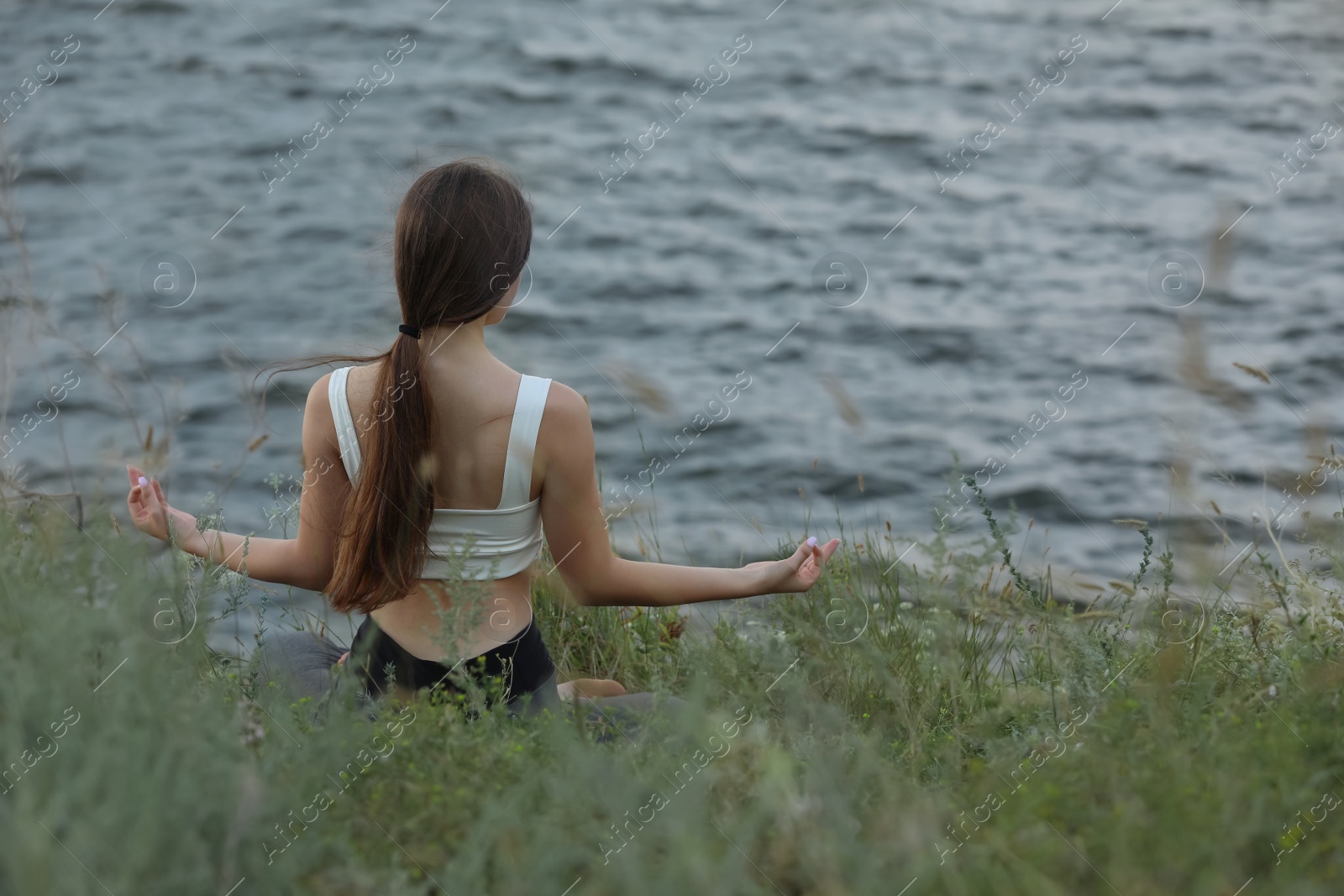 Photo of Teenage girl meditating near river, back view. Space for text
