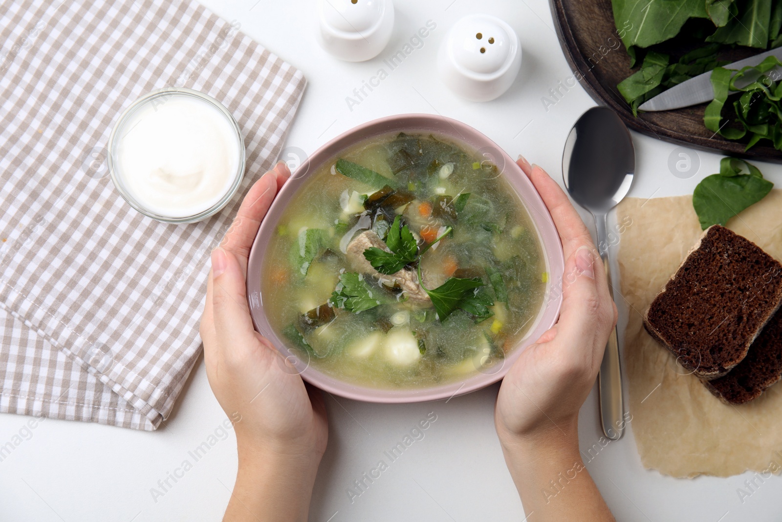 Photo of Woman eating delicious sorrel soup with meat and parsley at white table, top view