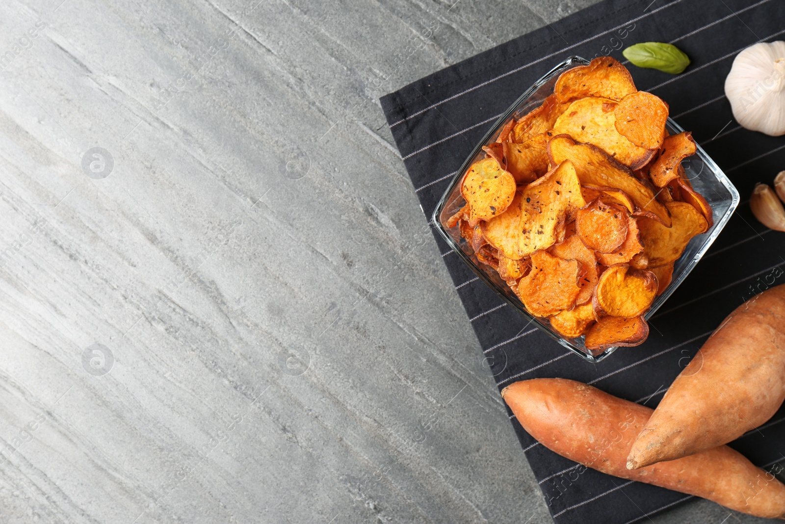 Photo of Flat lay composition with bowl of sweet potato chips on grey table. Space for text