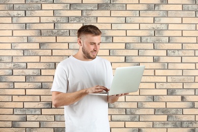 Photo of Young handsome man with laptop on brick wall background