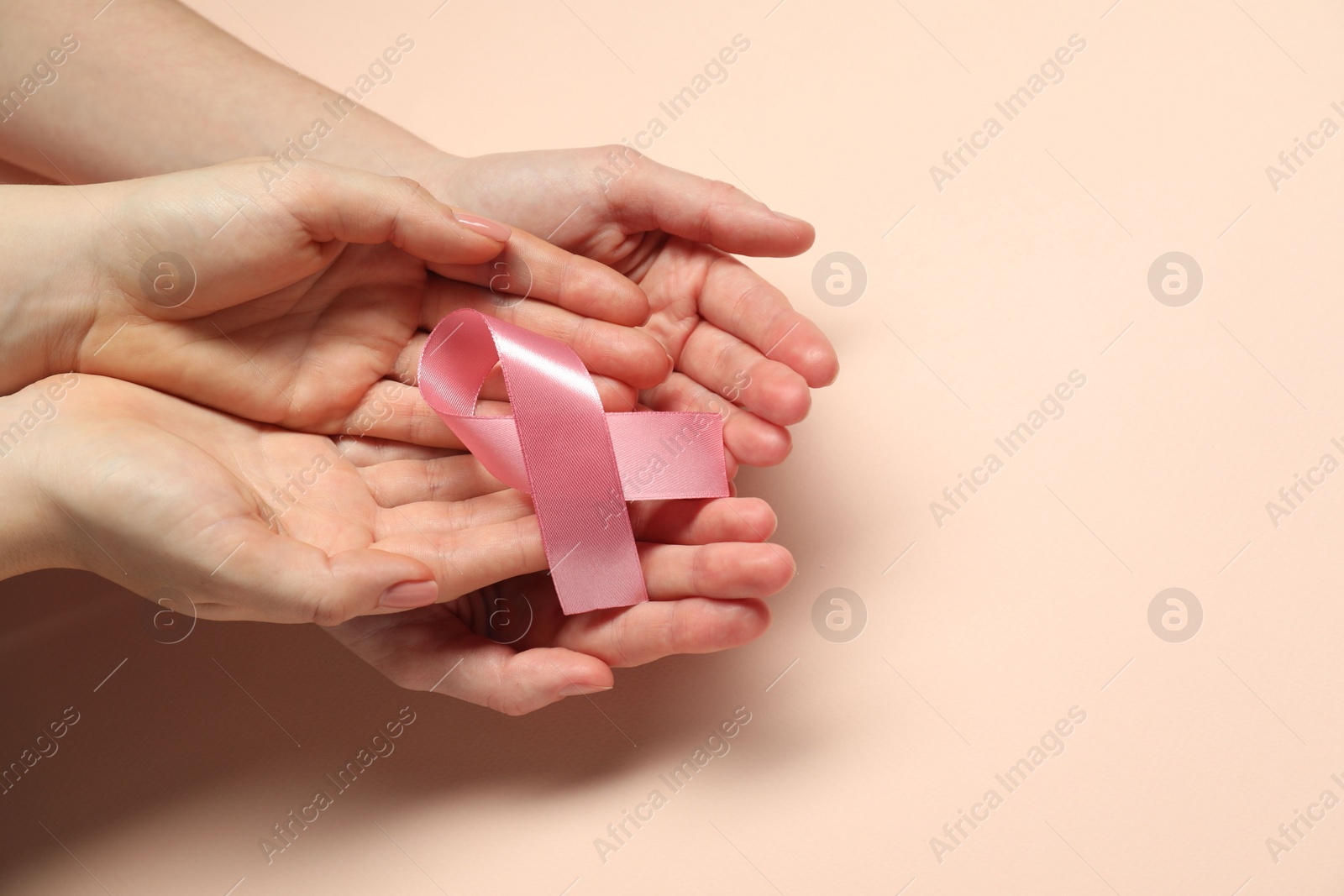 Photo of Breast cancer awareness. Women holding pink ribbon on beige background, top view. Space for text