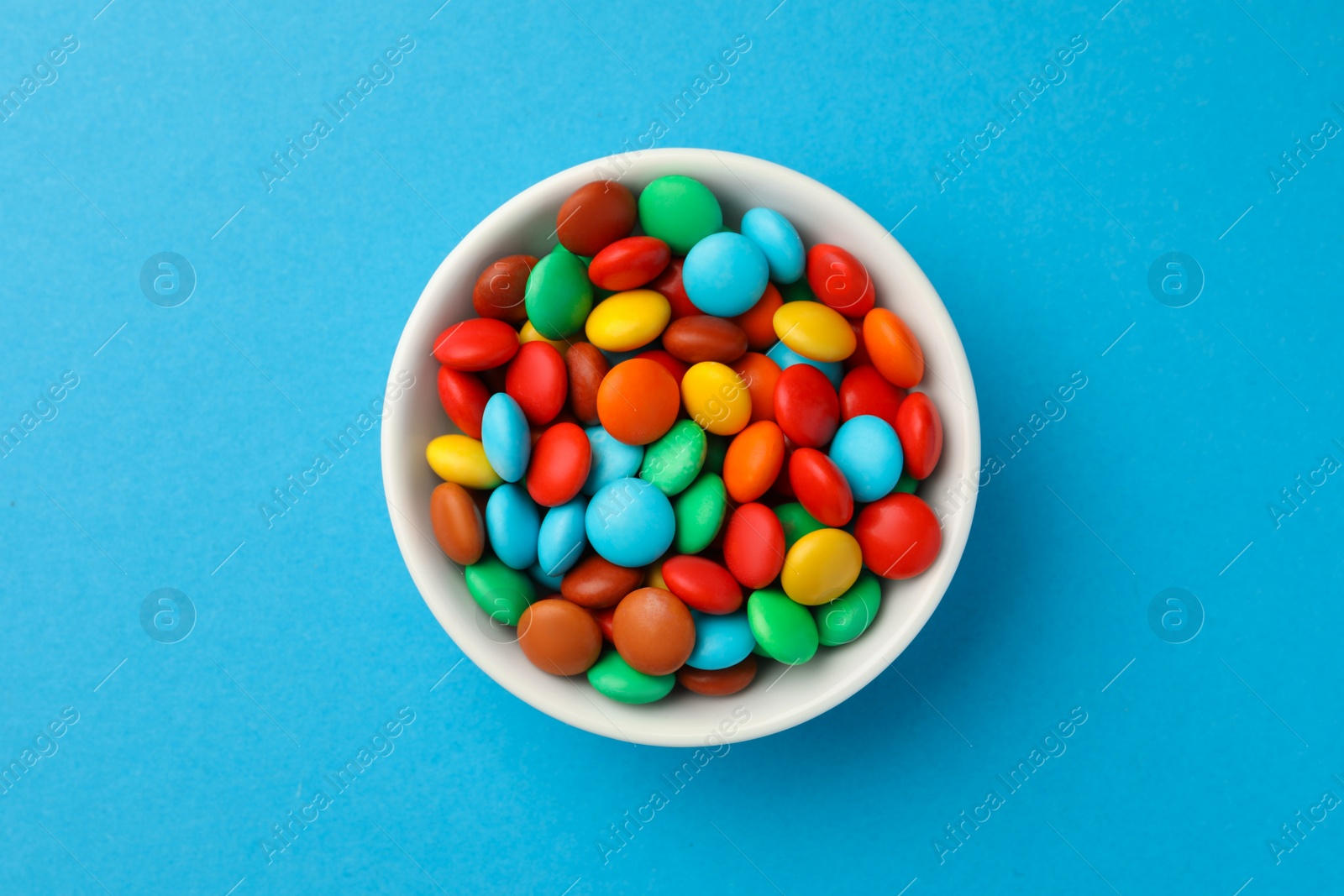 Photo of Bowl with tasty colorful candies on blue background, top view