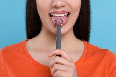 Photo of Woman brushing her tongue with cleaner on light blue background, closeup