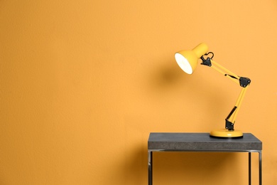 Photo of Stylish lamp on table against color background. Space for text