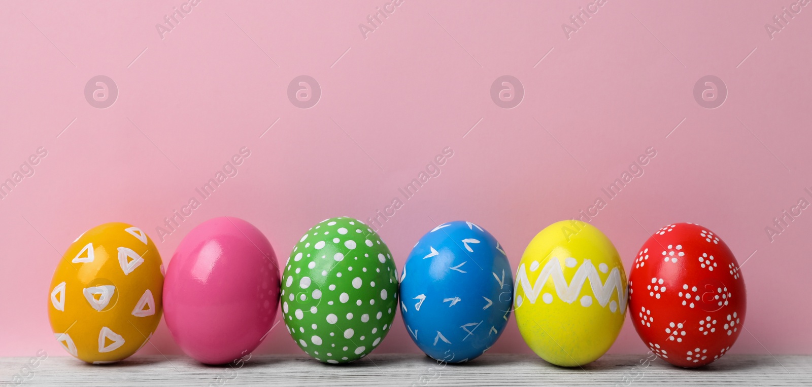 Photo of Decorated Easter eggs on table near color wall. Space for text