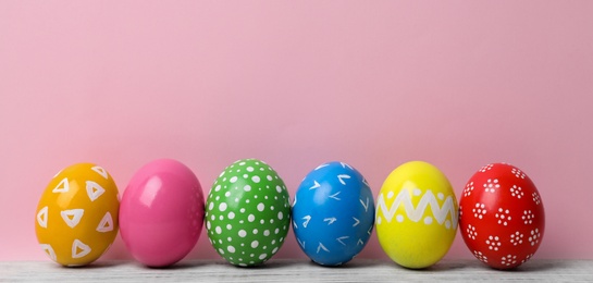 Decorated Easter eggs on table near color wall. Space for text