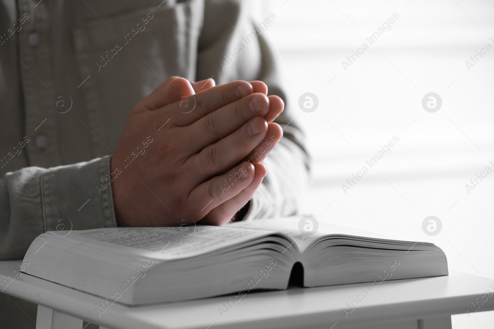 Photo of Religion. Christian man praying over Bible indoors, closeup