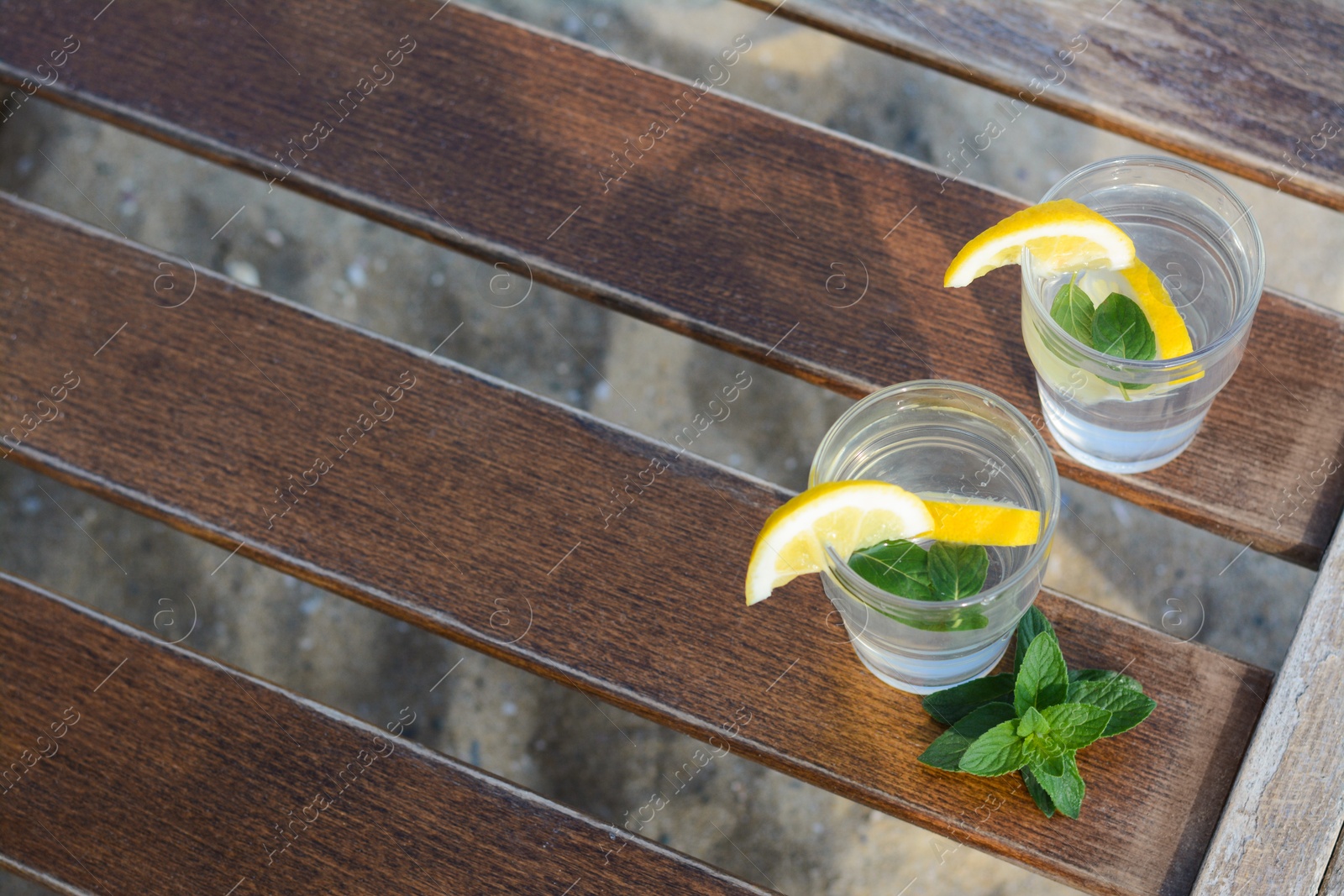 Photo of Refreshing water with lemon and mint on wooden table outdoors, above view. Space for text