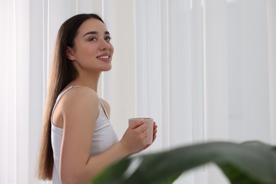 Photo of Happy woman with cup of drink near window indoors, space for text. Lazy morning