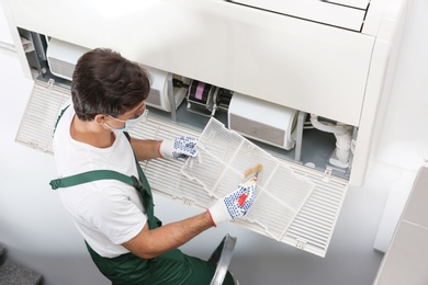 Photo of Young male technician cleaning air conditioner indoors