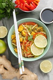 Photo of Stir-fry. Delicious cooked noodles with chicken and vegetables in bowl served on gray textured table, flat lay