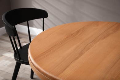 Round wooden table and black chair in room, closeup