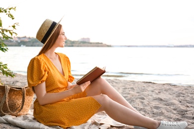 Photo of Young woman reading book on sandy beach near sea