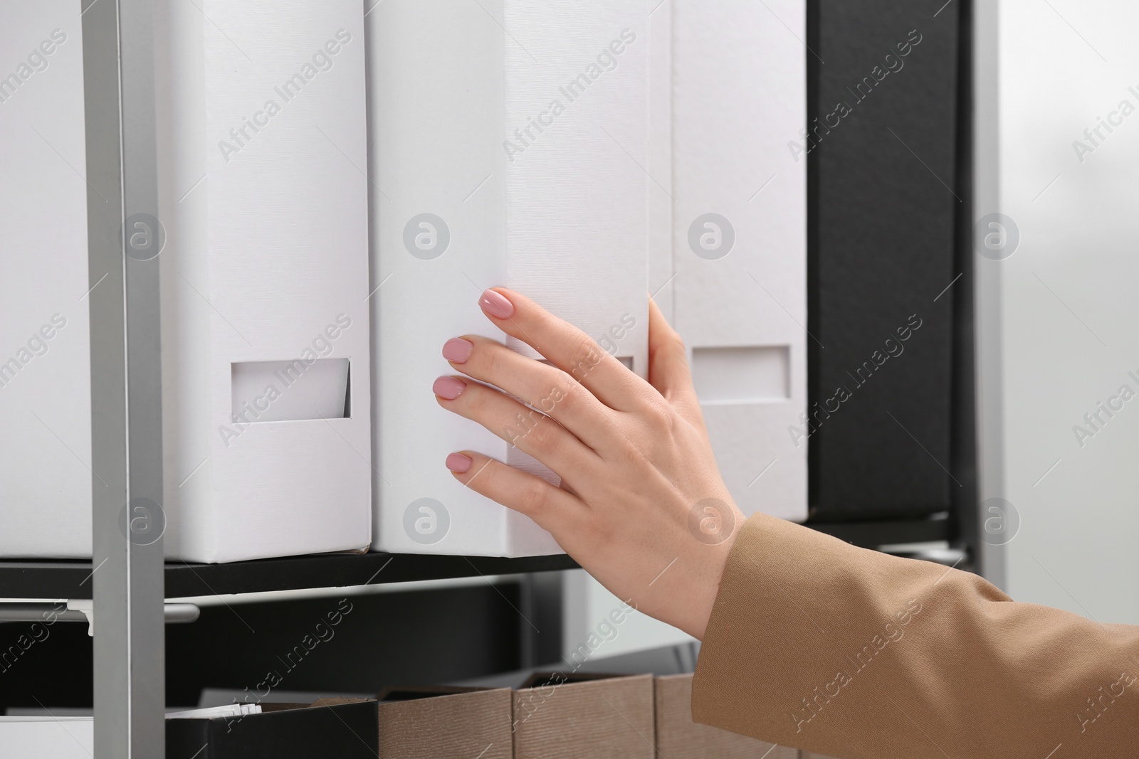 Photo of Woman taking folder with documents from shelf in office, closeup