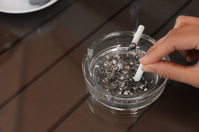 Woman putting out cigarette in ashtray at table, closeup