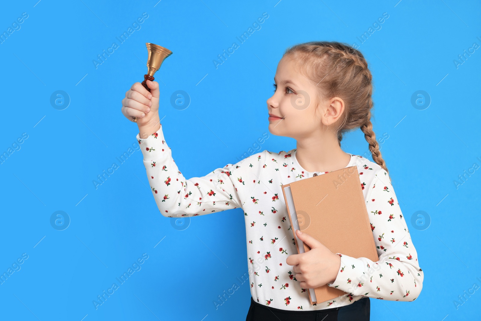 Photo of Pupil with school bell and book on light blue background