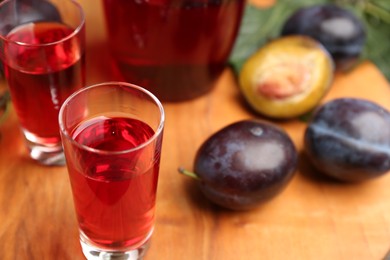 Photo of Delicious plum liquor in shot glass on wooden board. Homemade strong alcoholic beverage