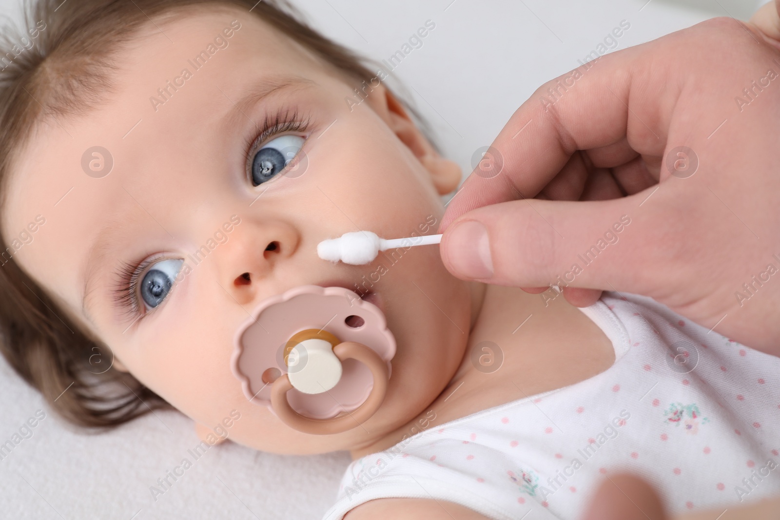 Photo of Father cleaning nose of his baby with cotton bud on bed, closeup