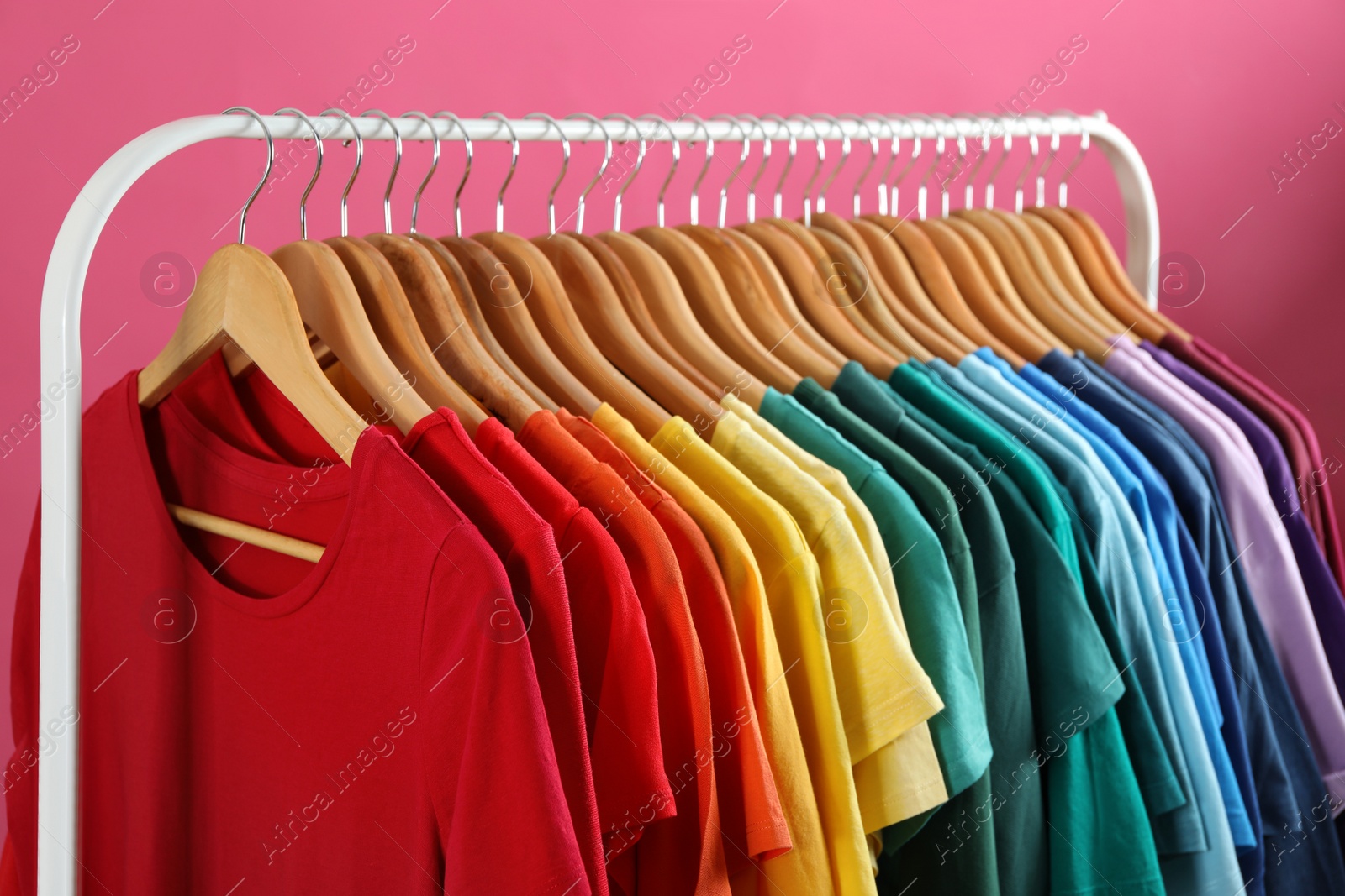 Photo of Rack with bright clothes on pink background. Rainbow colors