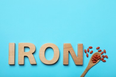 Photo of Word Iron and pills on light blue background, flat lay with space for text. Anemia treatment