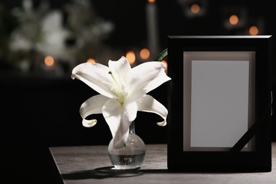 Photo of Funeral photo frame with black ribbon and lily on table in dark room