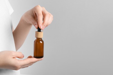 Woman holding bottle with serum against light grey background, closeup. Space for text