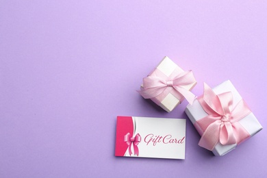 Photo of Gift card and presents on violet background, flat lay. Space for text