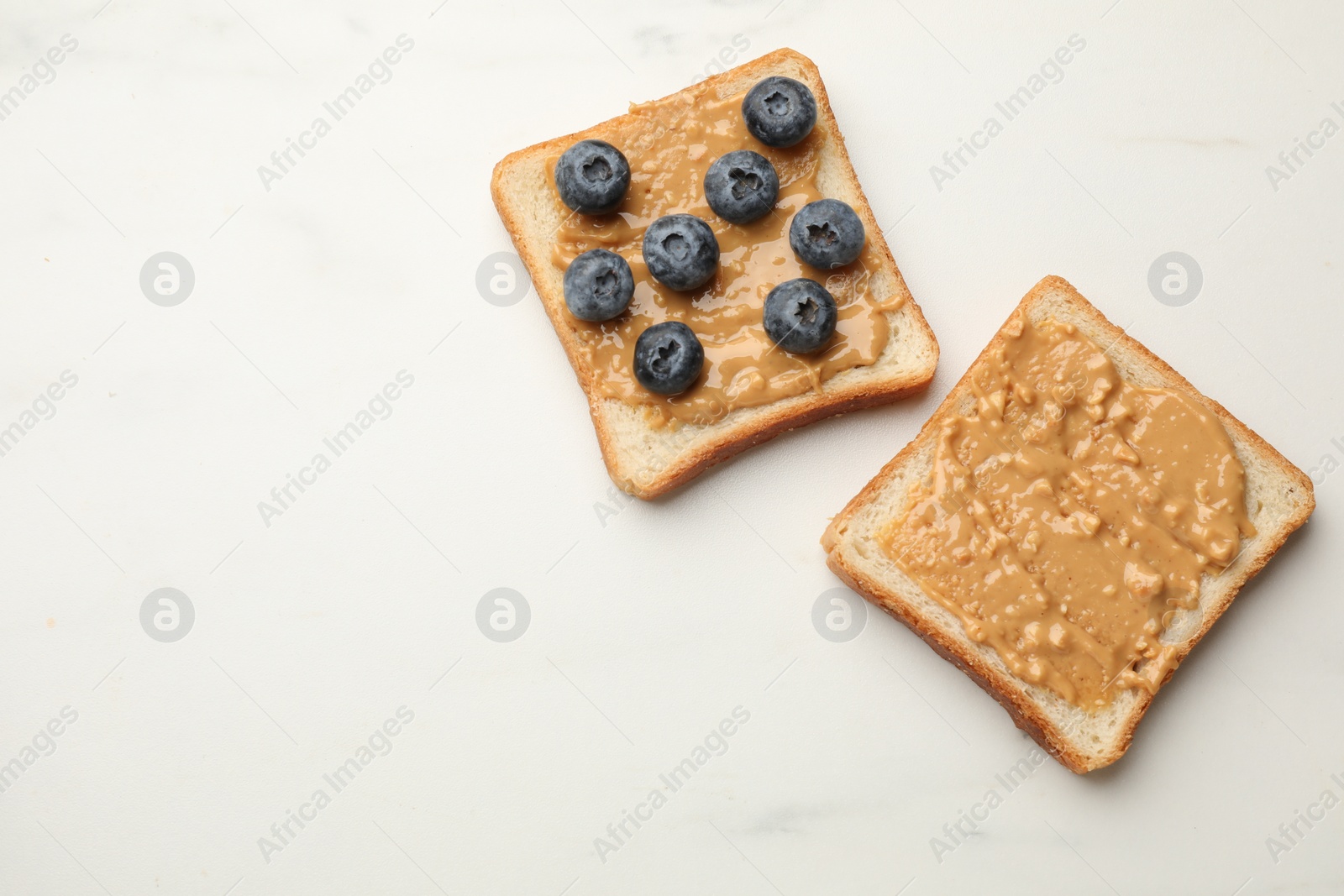 Photo of Delicious toasts with peanut butter and blueberries on white marble table, flat lay. Space for text