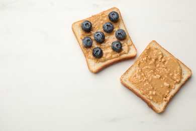 Photo of Delicious toasts with peanut butter and blueberries on white marble table, flat lay. Space for text