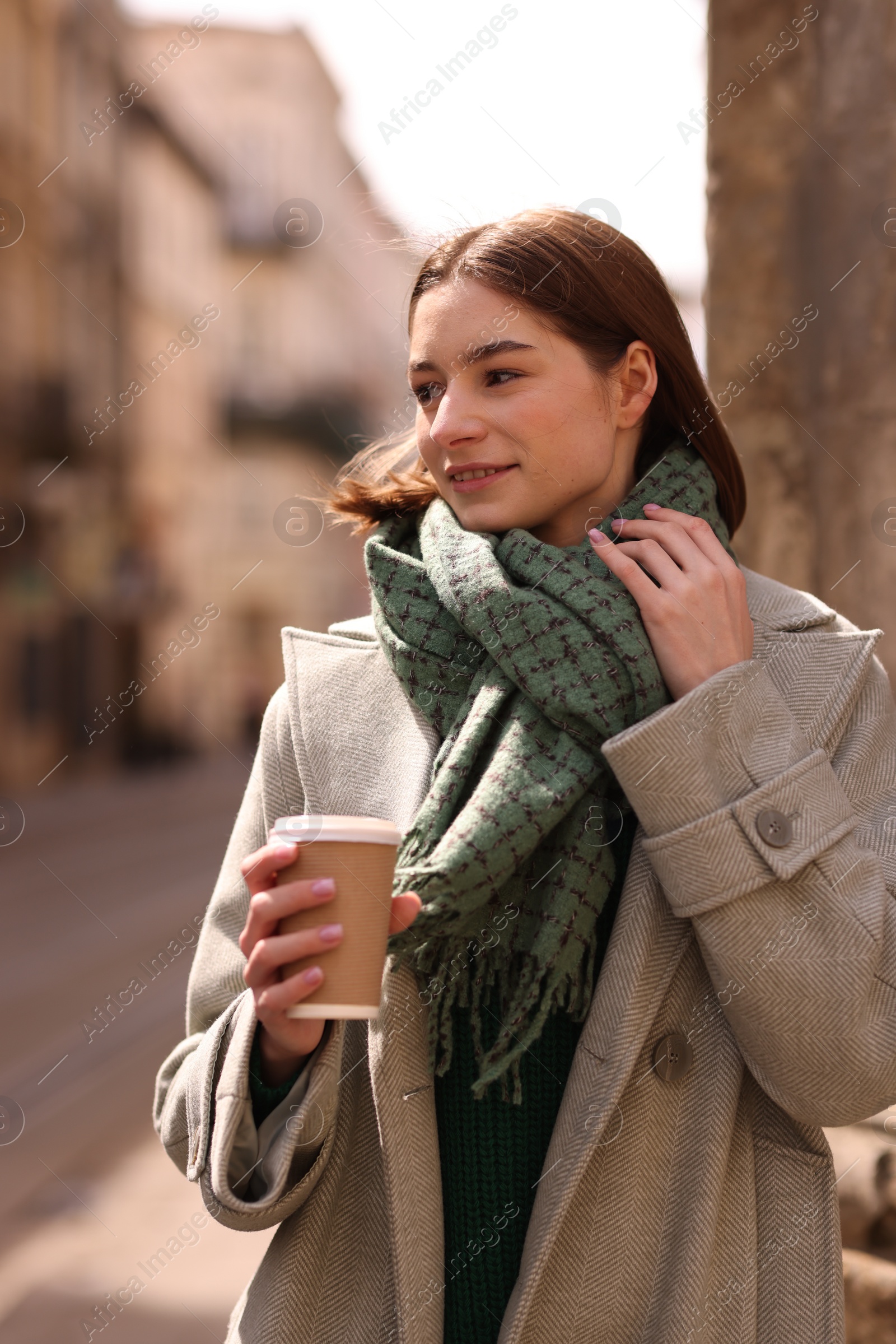 Photo of Beautiful woman in warm scarf with paper cup of coffee on city street