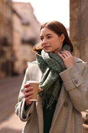 Beautiful woman in warm scarf with paper cup of coffee on city street