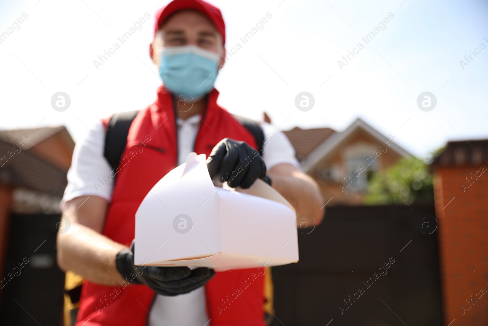 Photo of Courier in protective mask and gloves with order outdoors, focus on hands. Restaurant delivery service during coronavirus quarantine
