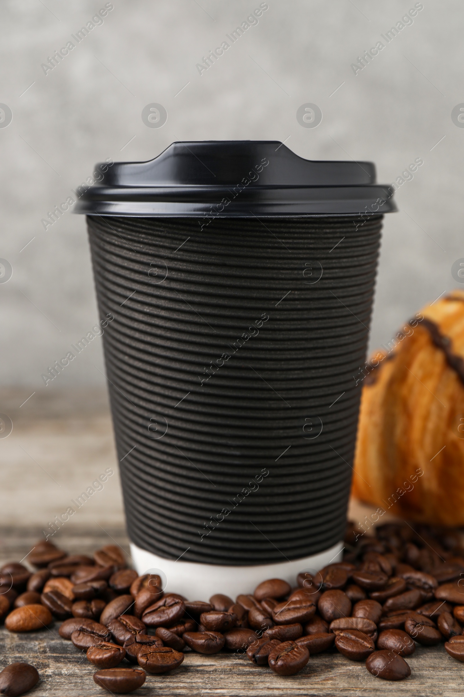 Photo of Coffee to go. Paper cup with tasty drink and beans on wooden table, closeup